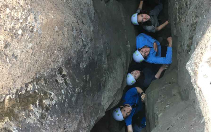 a group of students looks up and smile as they stand in a crevice between two rock walls